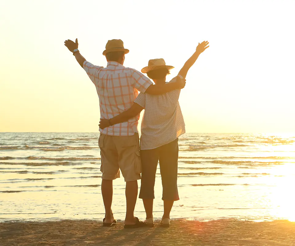 A couple raising their hands in front of the beach.