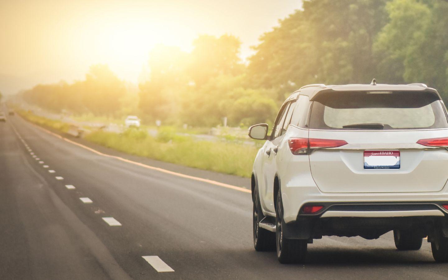 A white SUV driving on the highway toward the sunset.